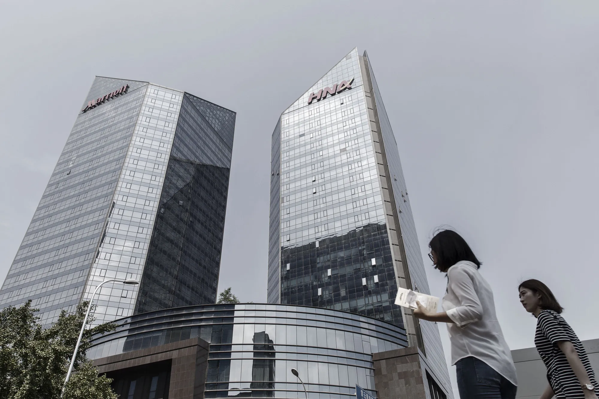 Pedestrians walk past the HNA Group Co. building in Beijing, China, on Wednesday, Aug. 9, 2017. Big Chinese dealmakers including HNA have been under increasing scrutiny this year as the Communist Party steps up its clampdown of capital outflows to protect the yuan from weakening further.