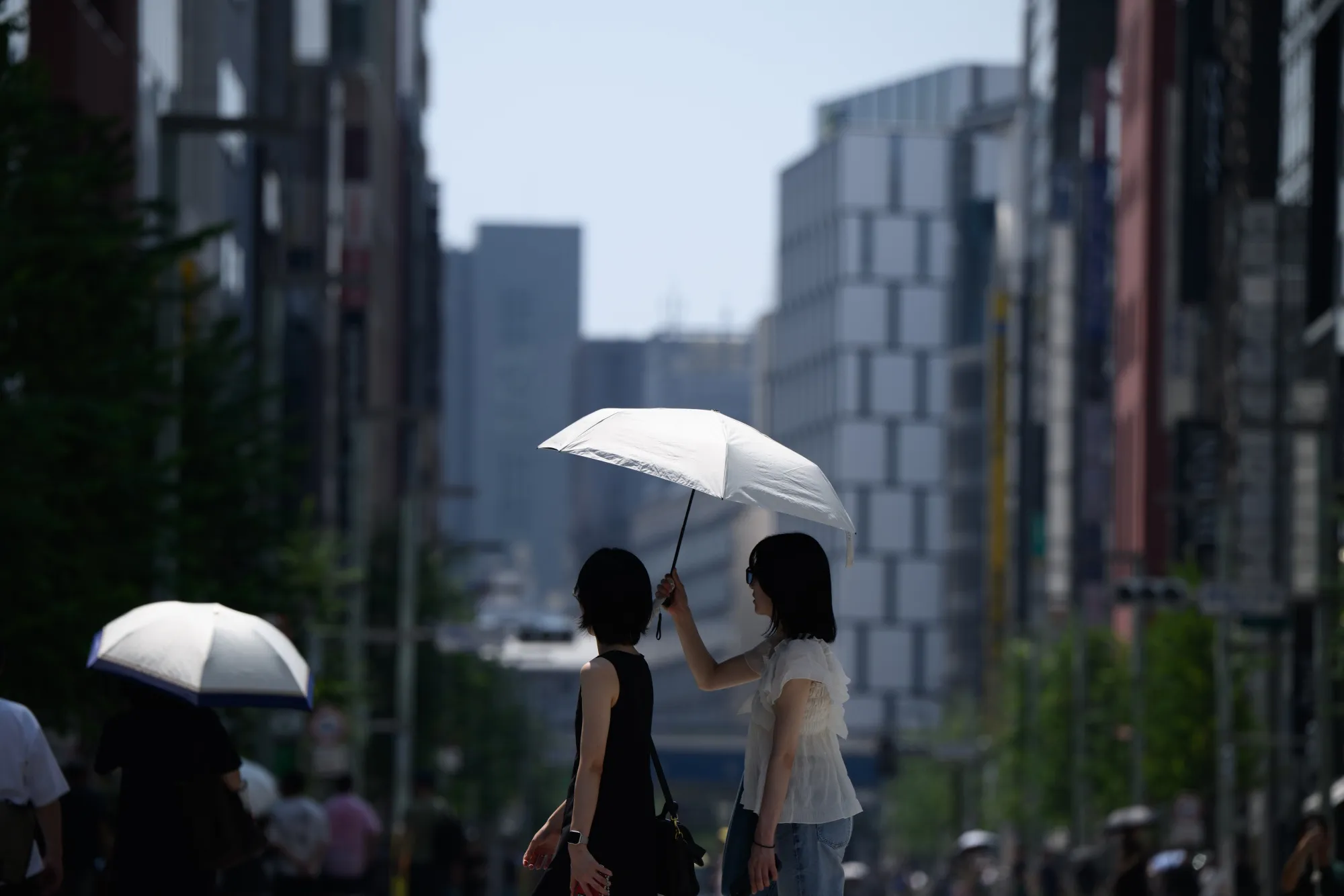Pedestrians share a parasol in Ginza district during high temperatures in Tokyo in August 2025.
