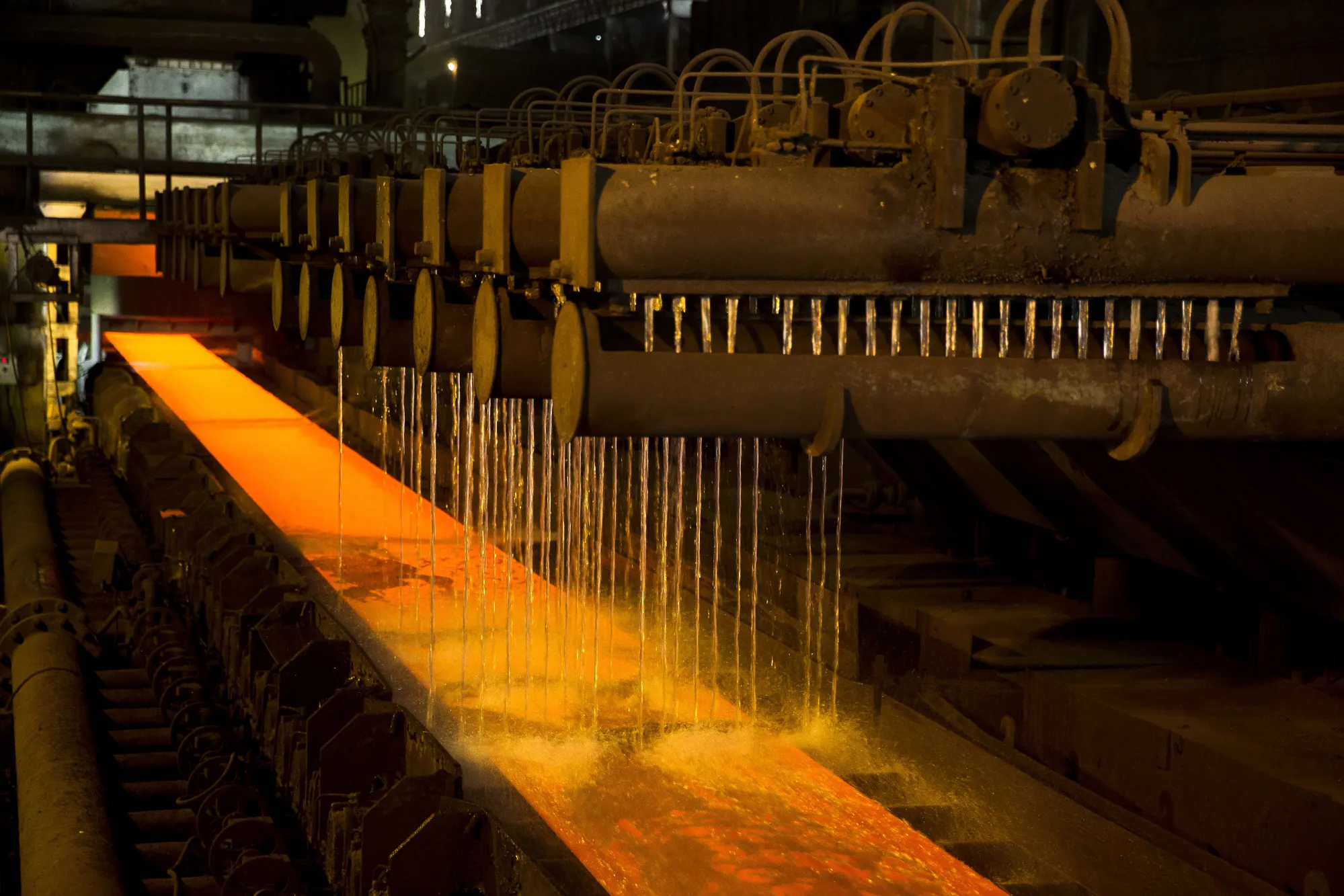 Cooling water pours onto a red hot steel slab at a factory.