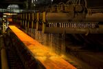Cooling water pours onto a red hot steel slab at a factory.