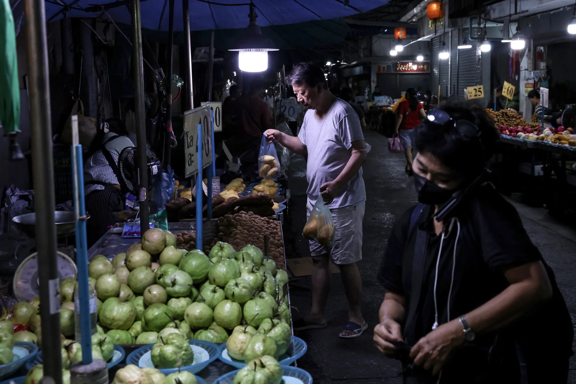 A customer buys produce at a market stall in Bangkok.