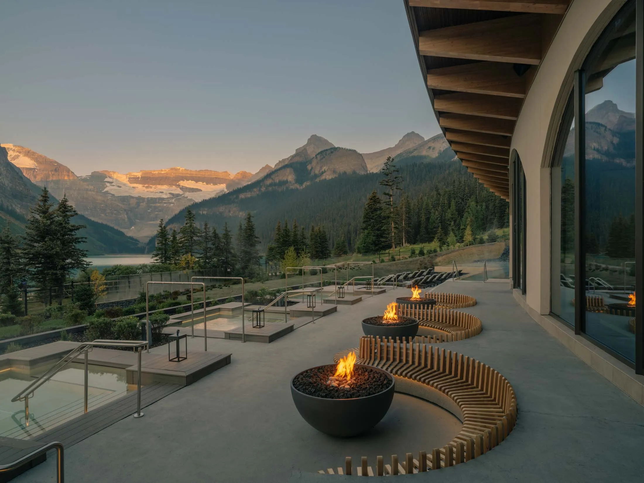 Exterior facade of a thermal spa facility with architectural benches around stylish fire pits, and views of the Canadian Rocky Mountains.