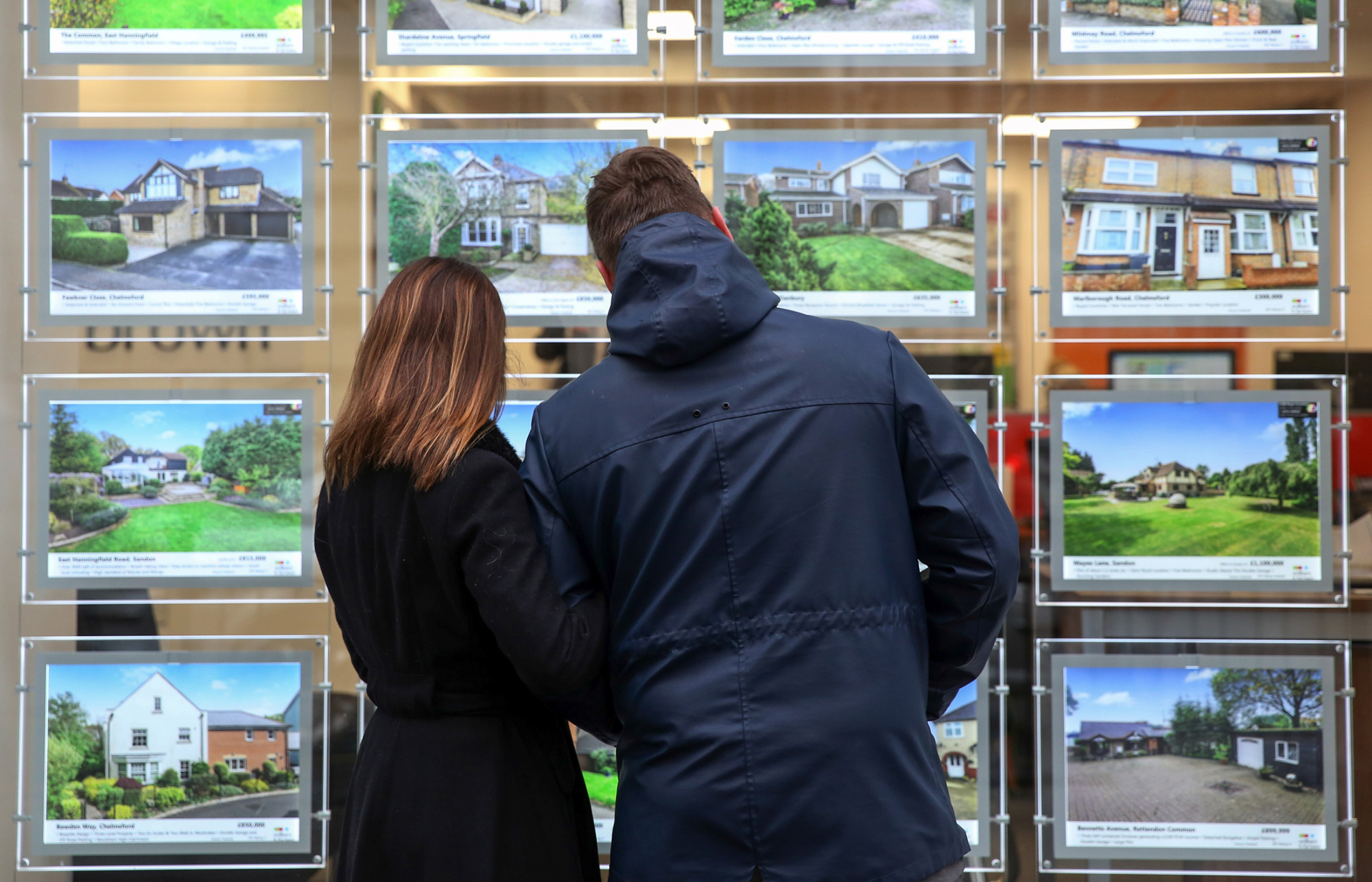 A couple look at houses for sale in the window of William H Brown estate agents in this arranged photograph in Chelmsford, U.K., on Tuesday, Dec. 15, 2015. U.K. asking prices rose an annual 7.4 percent in December amid a continuing shortage of homes for sale, according to Rightmove.
