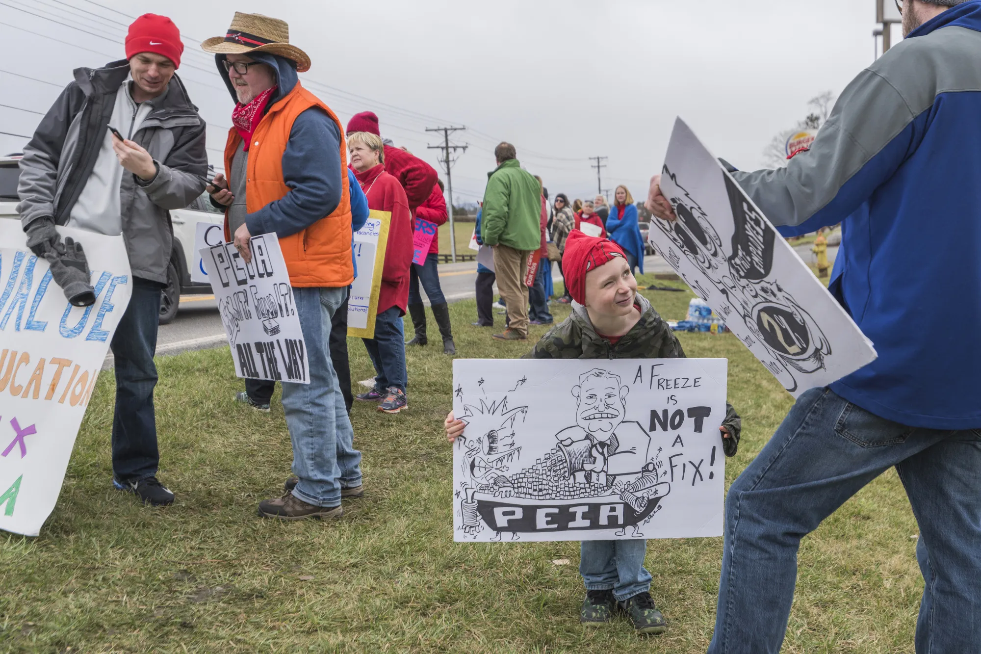 A boy makes a face at his father while holding a sign drawn by Lewisburg Elementary School art teacher Jody Wilber (in hat) during a demonstration in Lewisburg, West Virginia&nbsp;on&nbsp;Feb. 26, 2018.