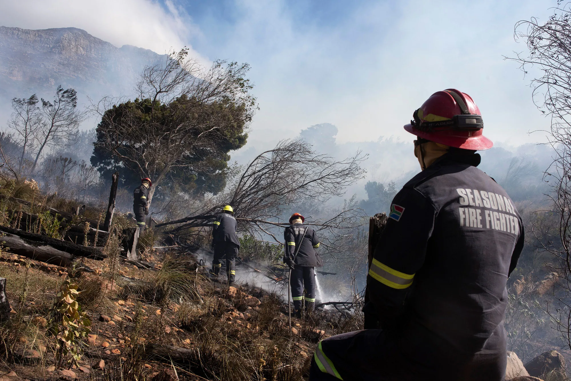 Fire-fighting teams dampen smoldering vegetation to control a forest fire on the foothills of Table Mountain in Cape Town on April 19.