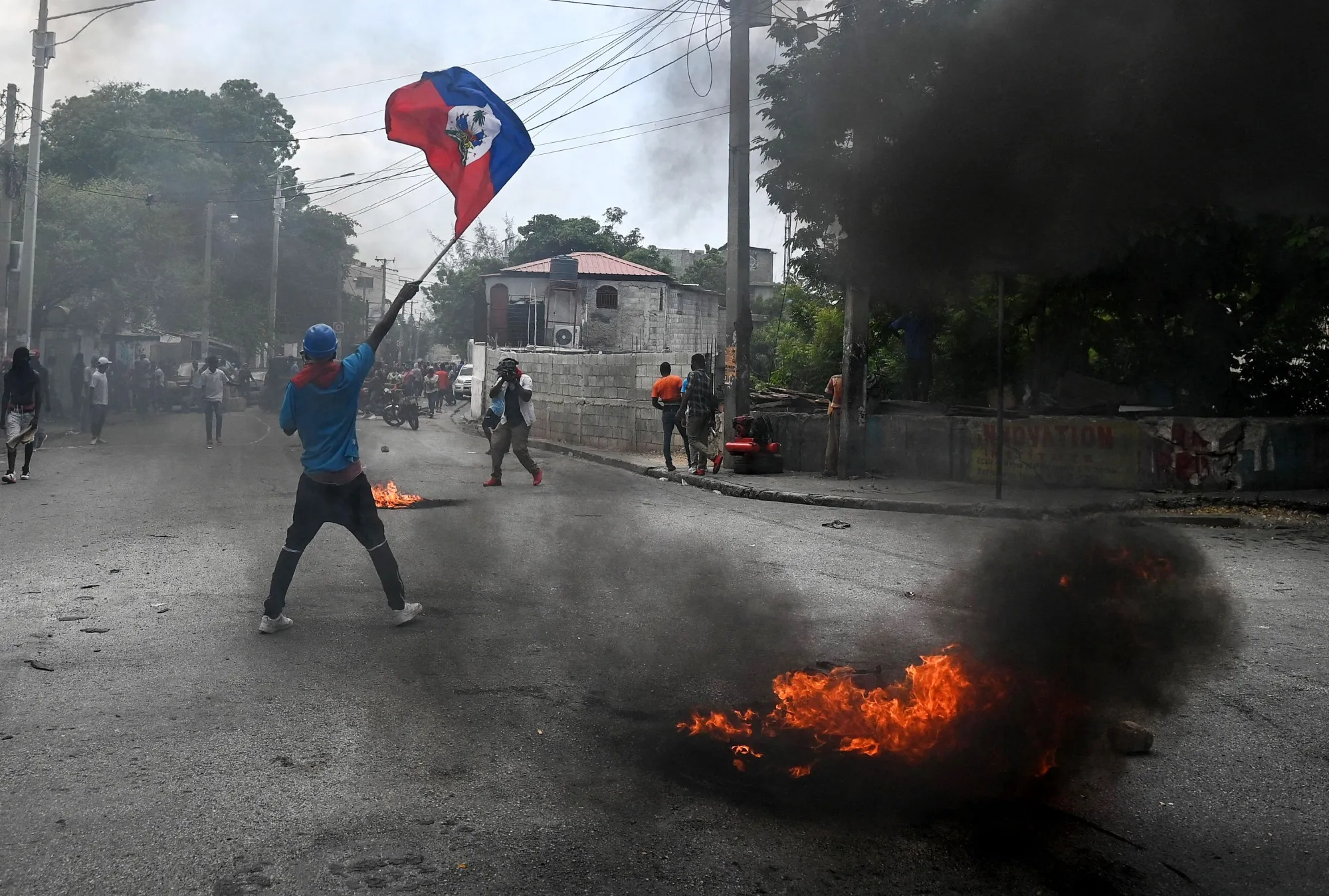 A man holds a Haitian flag as a tire burns during a demonstration in Port-au-Prince, Haiti.