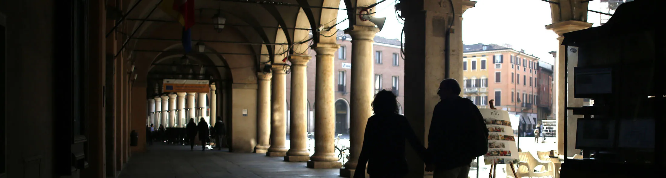 Pedestrians walk with a dog beneath arches at Piazza Grande in Modena, Italy, on Friday, March 7, 2014. Banca Popolare dell'Emilia Romagna SC is planning to repay this year about half of the 4.5 billion euros in funds obtained from the ECB in its three-year long-term refinancing operations. Photographer Alessia Pierdomenico/Bloomberg
