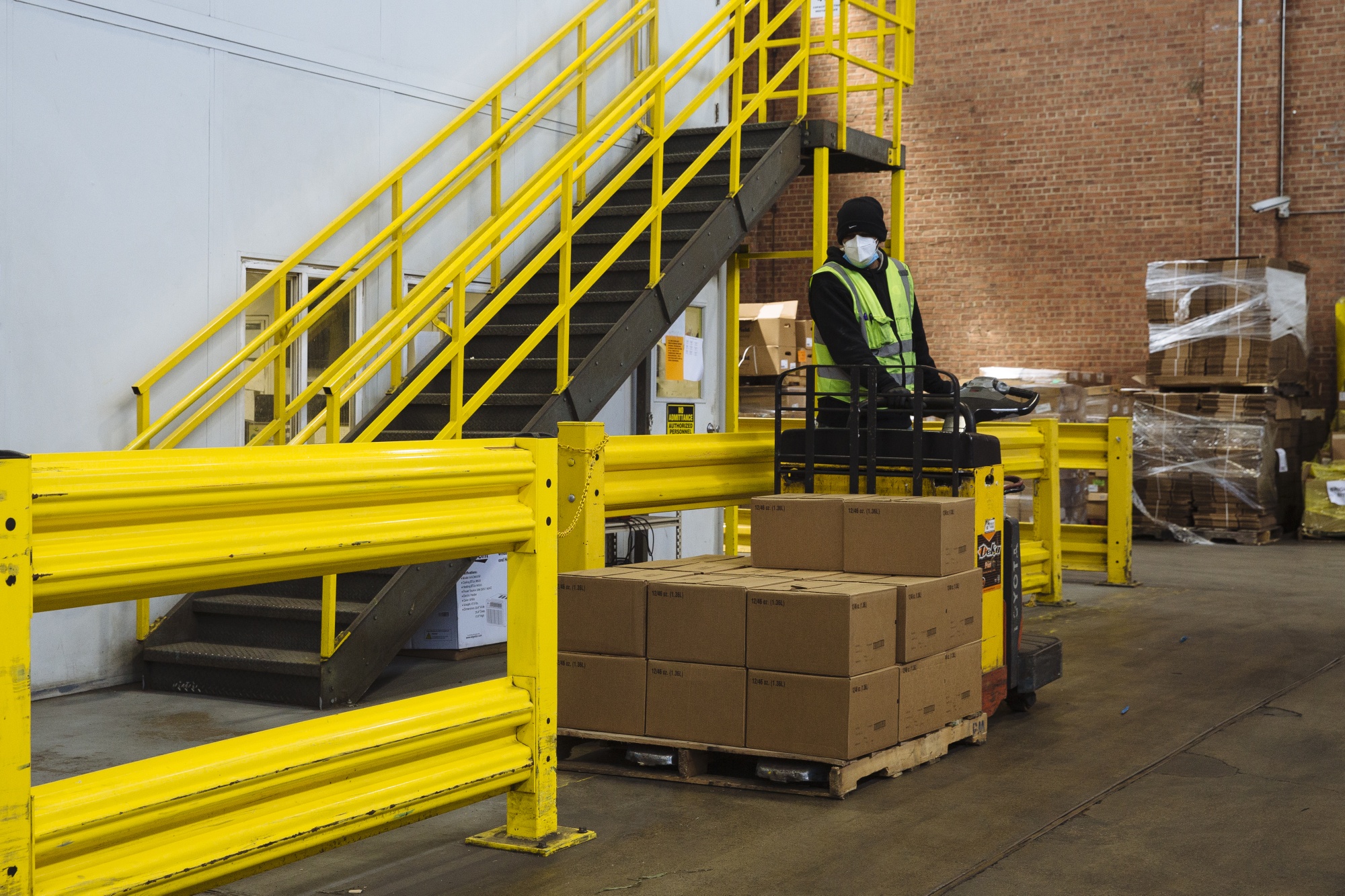 A worker wearing a protective mask and gloves operates a forklift while moving a pallet stacked with boxes of food at a City Harvest facility in New York, on May 7.