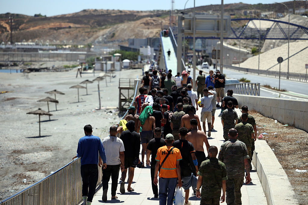 A group of migrants approach the border post to make their way back to Morocco, escorted by Spanish infantry soldiers, in the Spain’s north African enclave of Ceuta, on August 2, 2026. Photographer: HENRY NICHOLLS/AFP