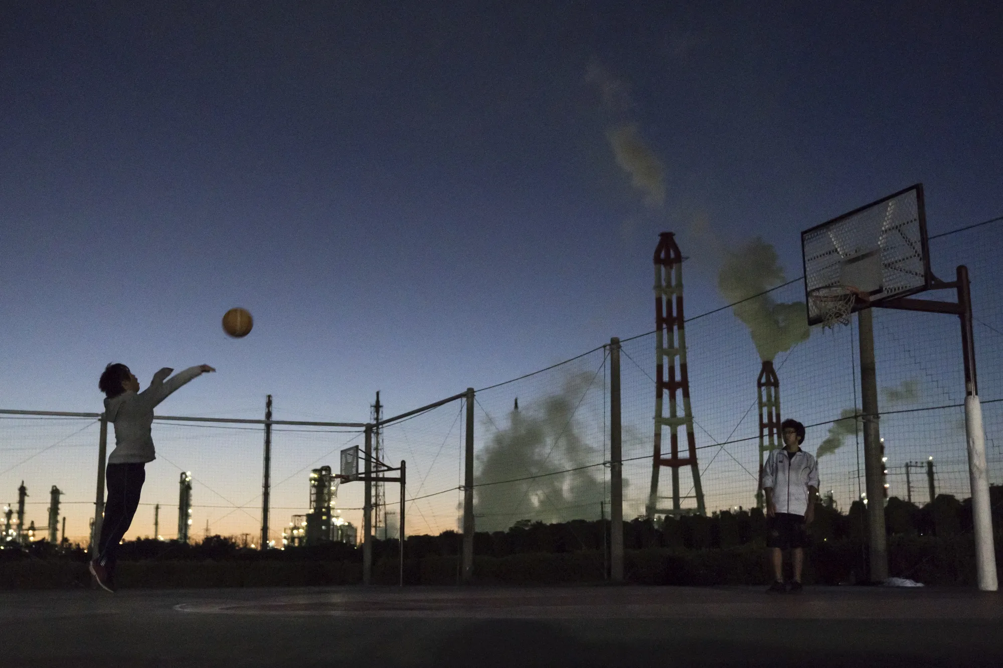 Men play basketball in front of factories at dusk in&nbsp;Ibaraki, Japan.&nbsp;