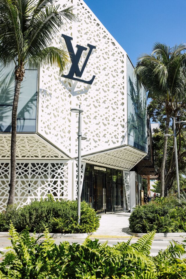 The exterior of a Louis Vuitton store with a a white facade next to palm trees. 