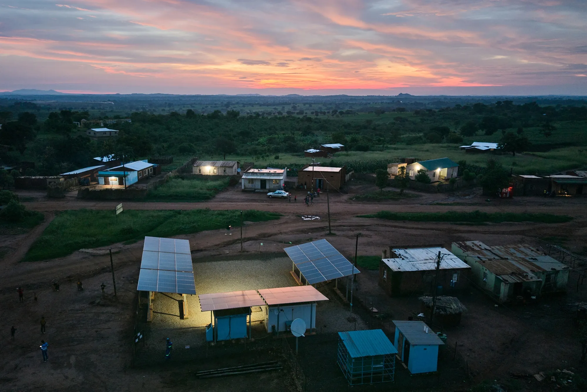 Rooftop solar panels power homes and buildings in Chitandika village, Zambia, with farmland and hills visible in the background.
