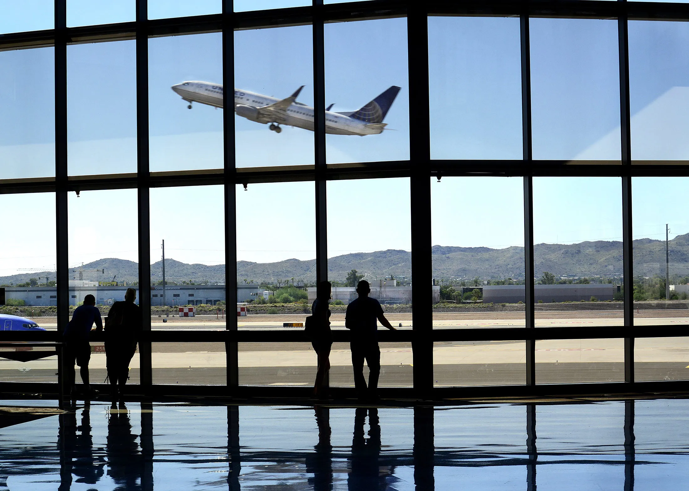 Airline passengers waiting for their flights watch from the terminal as a United Airlines airplane takes off at Phoenix Sky Harbor International Airport in Phoenix, Arizona.
