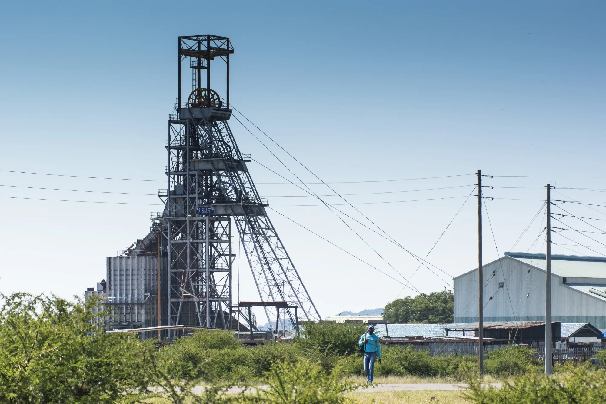 A pedestrian walks along a street as the Impala Platinum Holdings Ltd. shaft 9 mine tower stands beyond in Rustenburg.