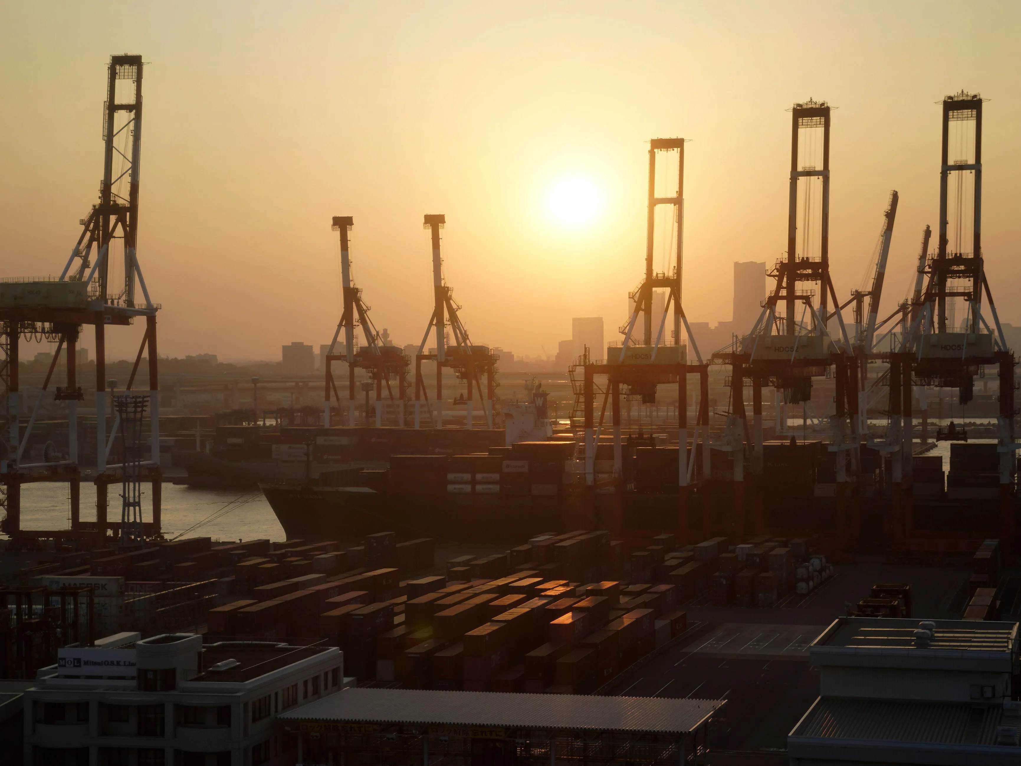 Containers sit next to gantry cranes as the sun sets at a shipping terminal at dusk in Yokohama, Japan