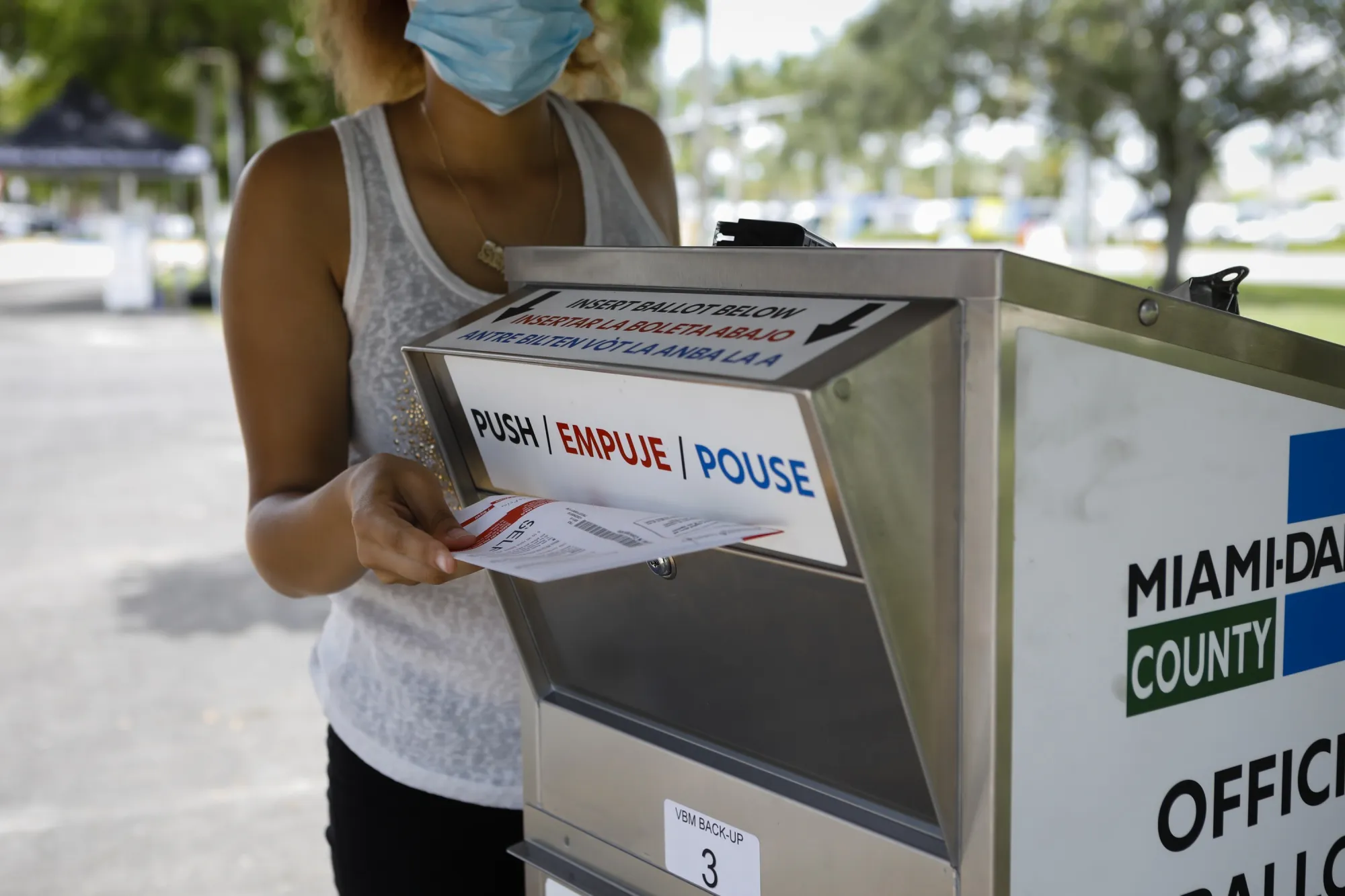 An election official wearing a protective mask drops off a mail-in ballot in a drop box at a polling location in Miami on Aug. 18, 2020.