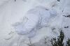 A US soldier, dressed in all white, is partially buried in snow. Her body appears relaxed and, if we didn’t know this was part of a military training exercise, we would think she is napping comfortably on her side. The soldier blends in with her surroundings and there is a spray of evergreen branches poking through on the bottom right of the image.