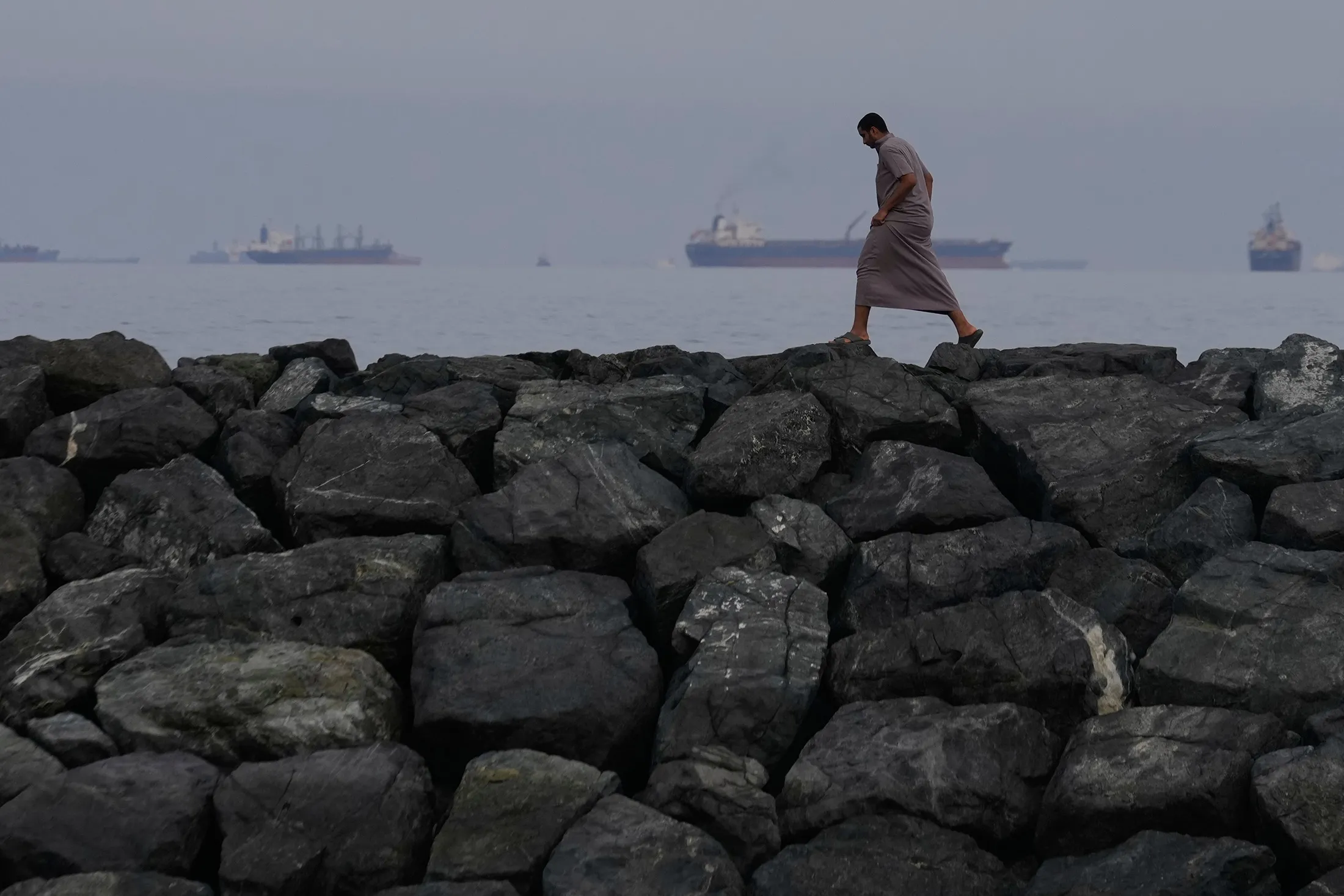 A man walks along the shore as oil tankers and cargo ships line up in the Strait of Hormuz, in Khor Fakkan, United Arab Emirates, on&nbsp;March 11.