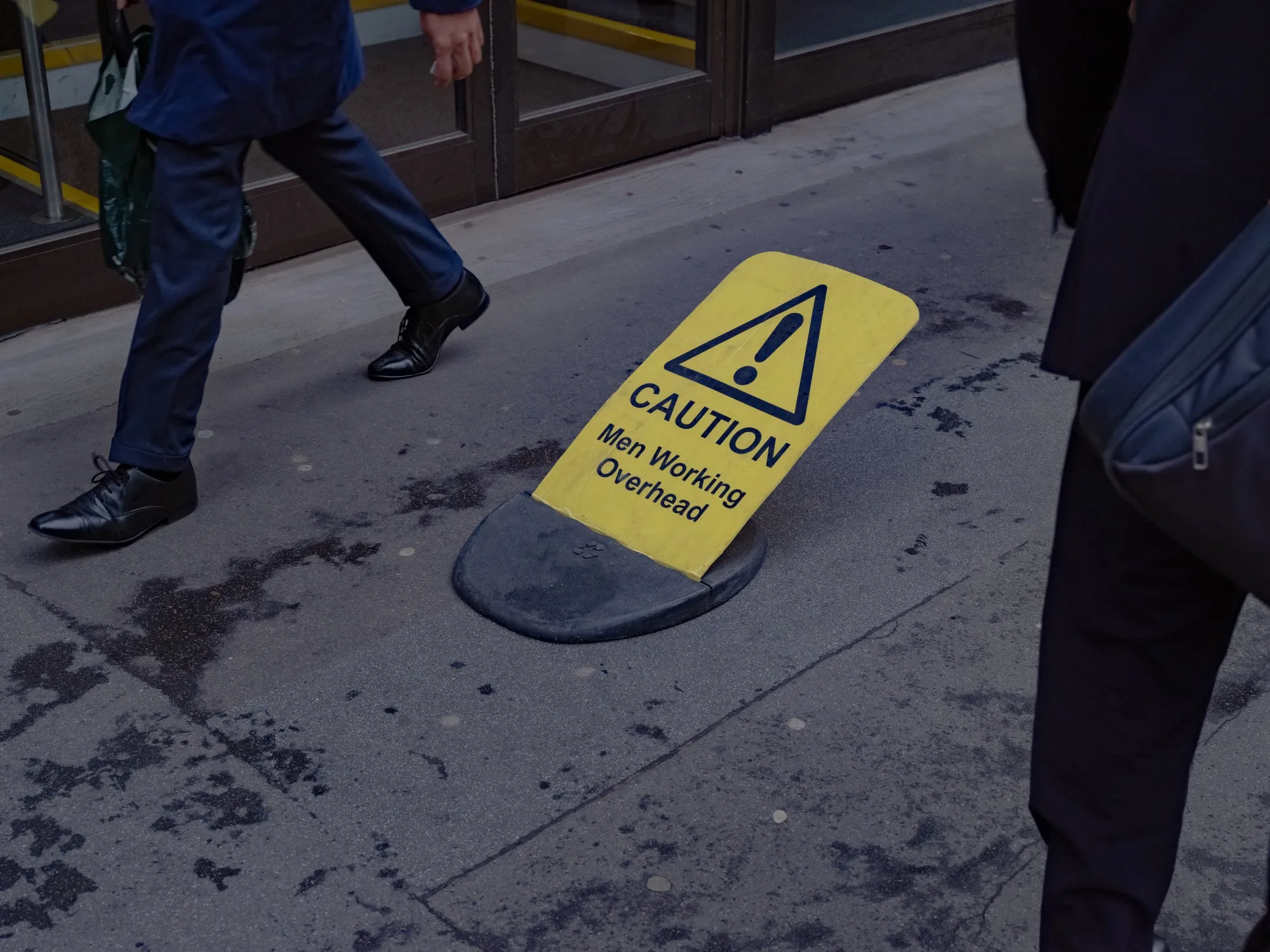 Office workers walk around a 'Men Working Overhead' warning sign in the City of London, UK.
