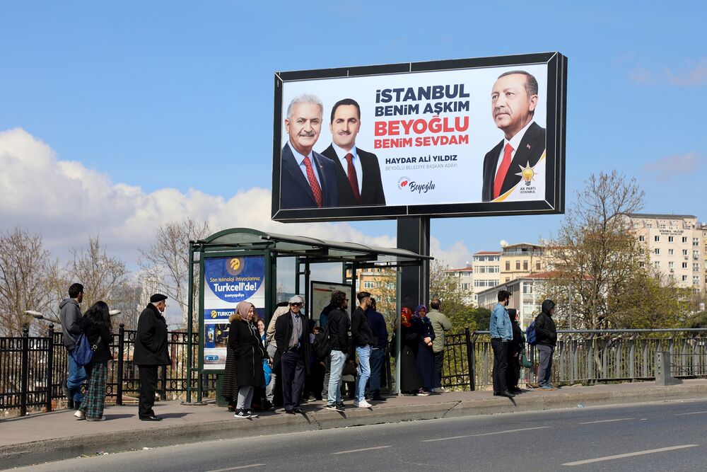 Pedestrians stand beneath an electoral board for the AK Party featuring Erdogan.