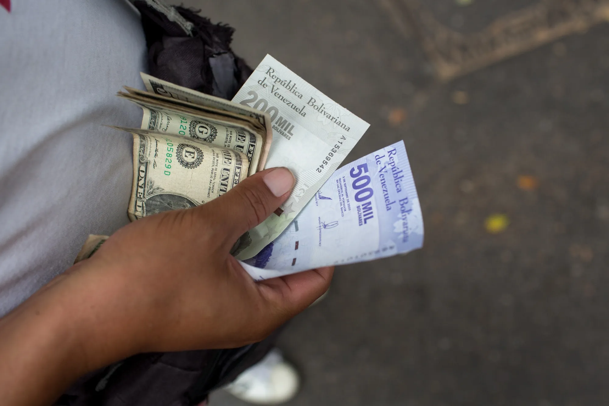 A bus worker holds US dollars and bolivar banknotes in Caracas, Venezuela.