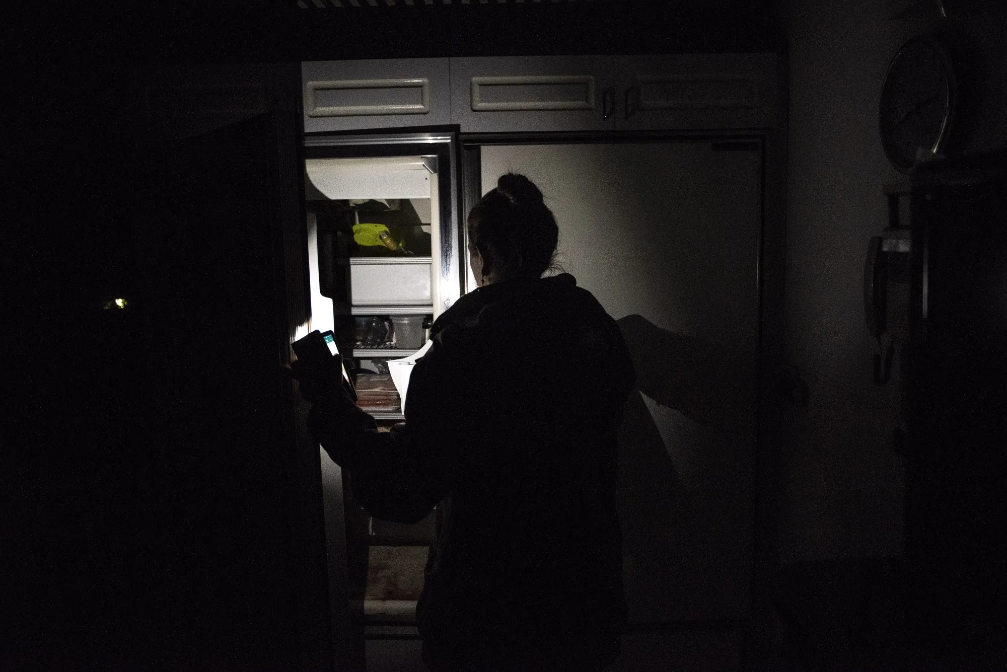 A person uses the light from a cellphone to view food inside a refrigerator during a power outage in Caracas on March 25, 2019.
