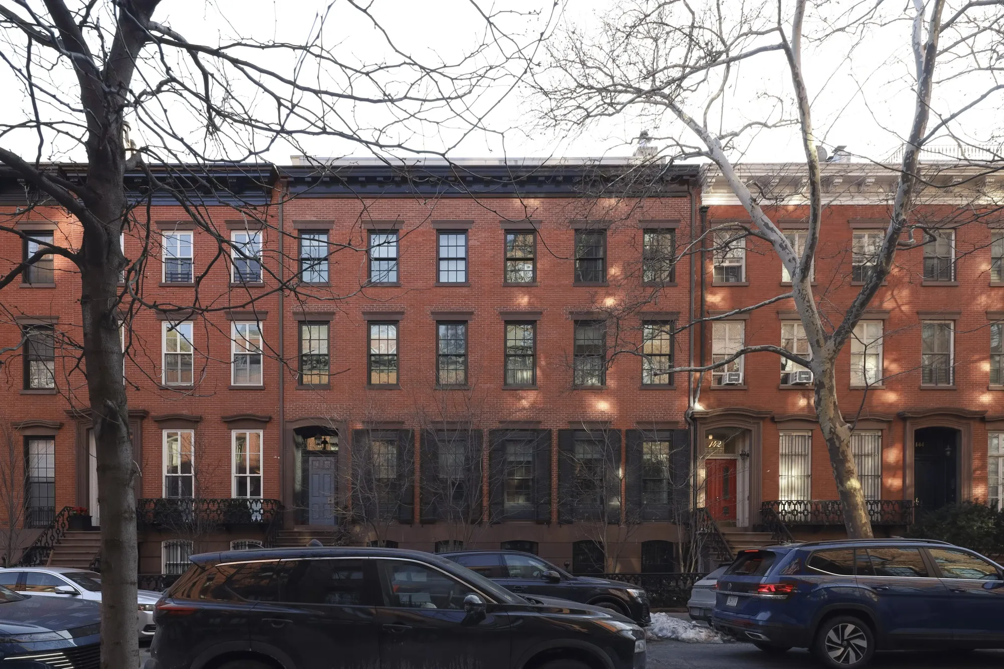 A red brick mega-mansion with a historic facade, cars parked in front of it on the street.