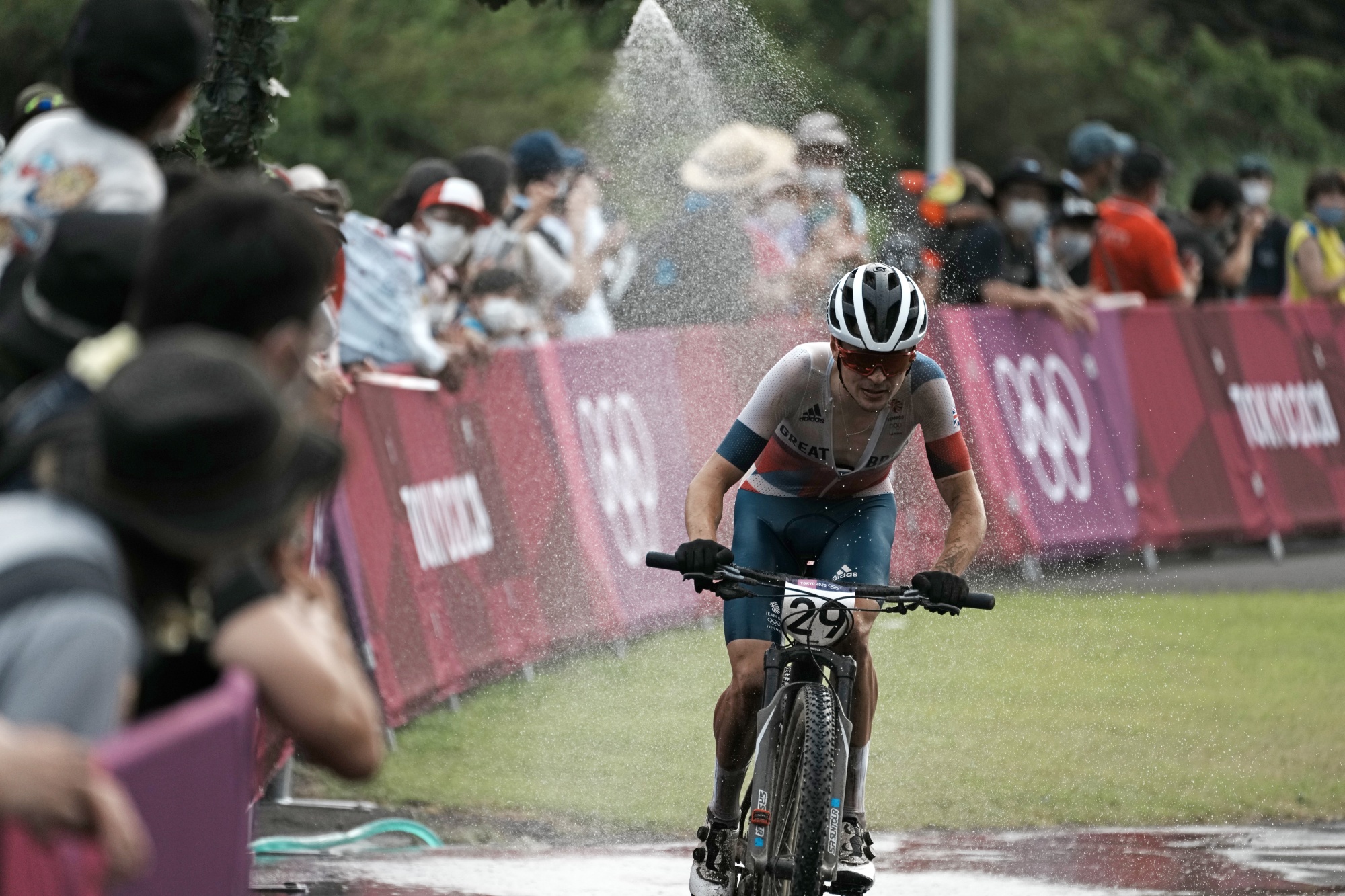 Photo showing Btirish cyclist Thomas Pidcock competing during the men's cross country mountain bike competition. There was water being sprayed onto him.