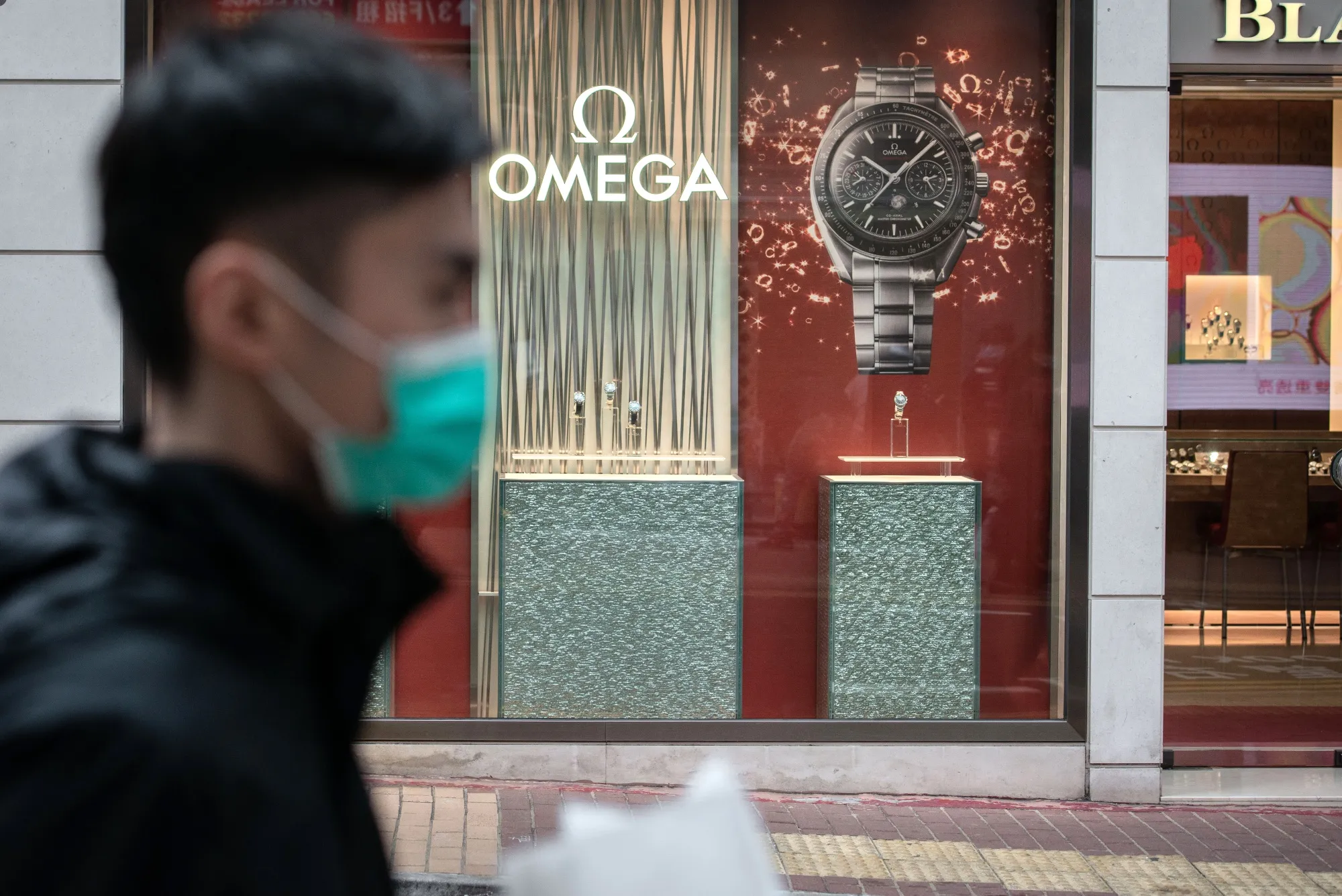 A pedestrian wearing a protective mask walks past an Omega SA store in&nbsp;Hong Kong.