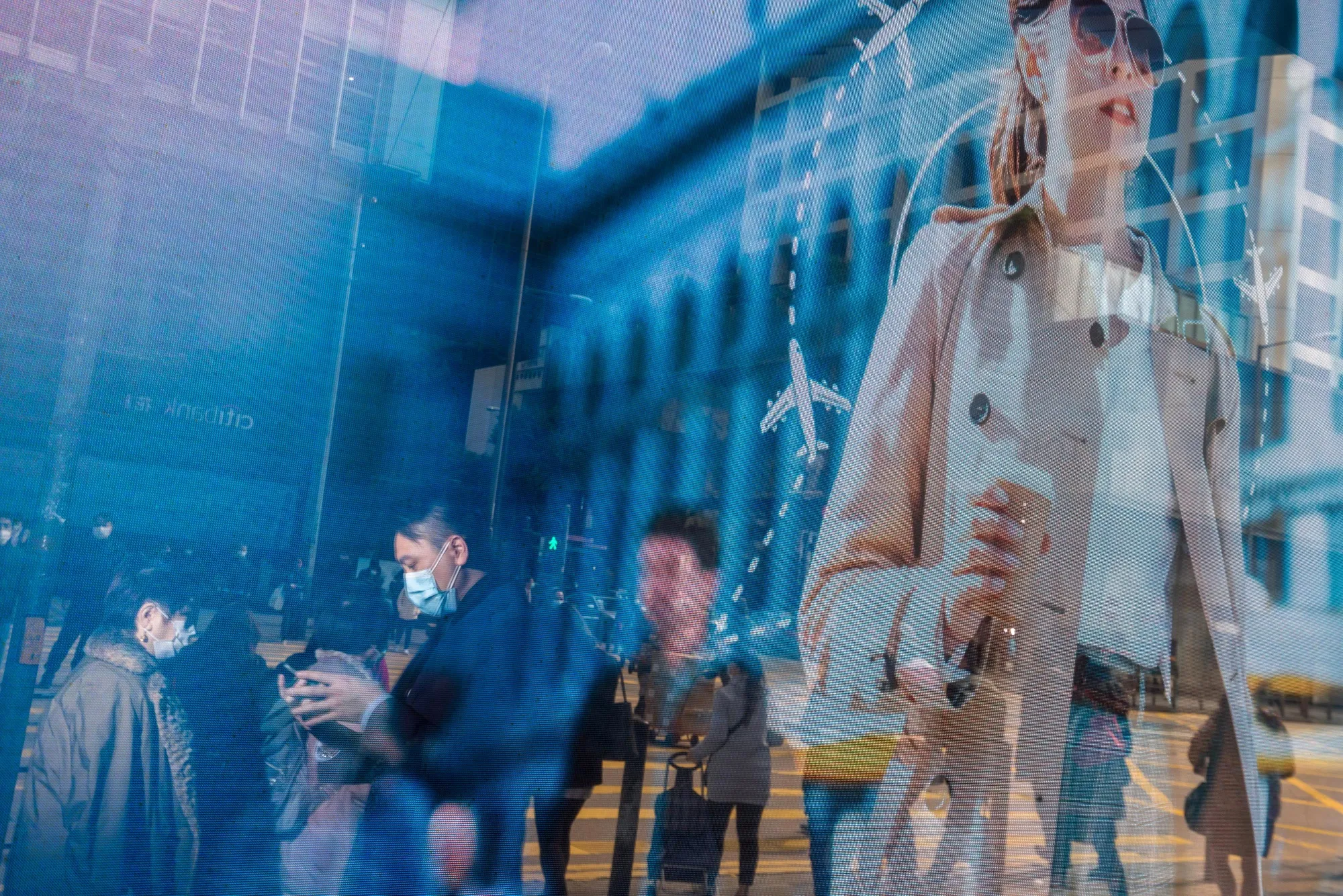 Pedestrians wearing protective masks are reflected in an advertisement in the Central district of Hong Kong.