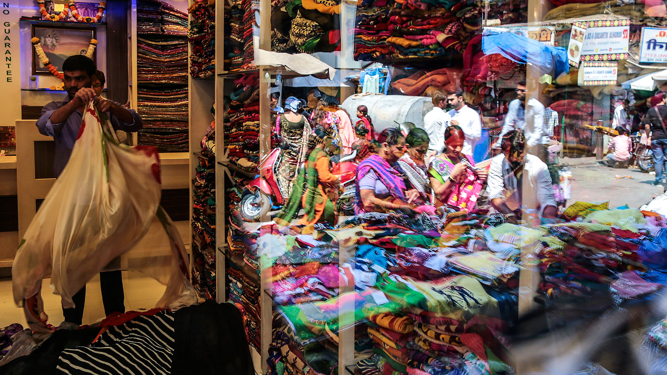 Customers browsing at a fabric stall are reflected in a store window at Mangaldas Market in Mumbai, India, on Feb. 26, 2015.
