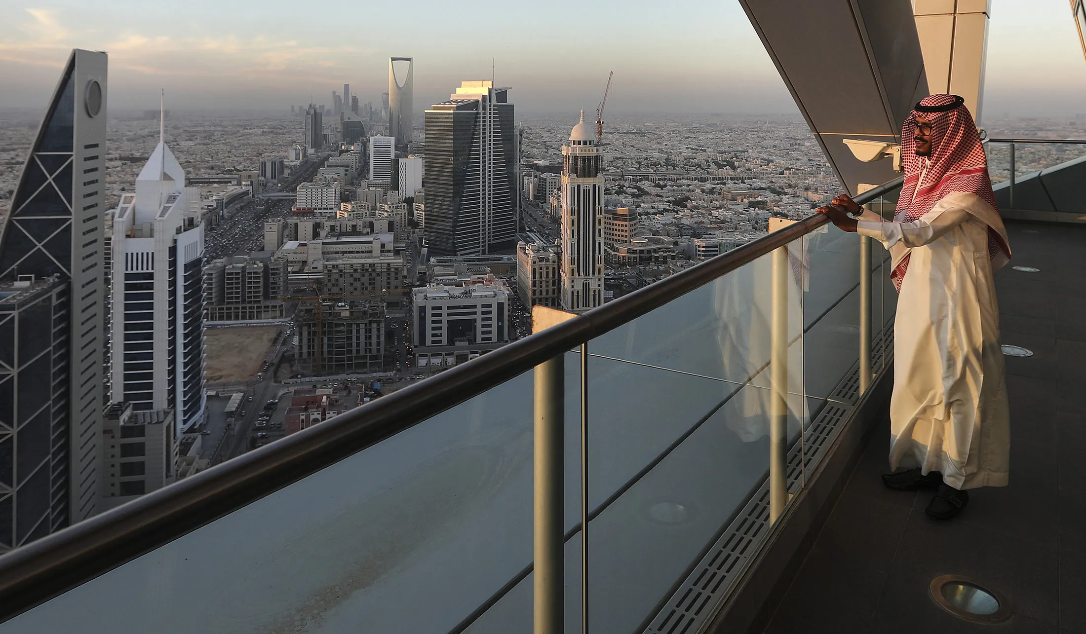 An employee looks out from the 32nd floor viewing platform of the Al Faisaliah Tower, as skyscrapers and commercial buildings stand beyond, in Riyadh, Saudi Arabia, on Thursday, Dec. 1, 2016. Saudi Arabia is working to reduce the Middle East’s biggest economy’s reliance on oil, which provides three-quarters of government revenue, as part of a plan for the biggest economic shakeup since the country’s founding.
