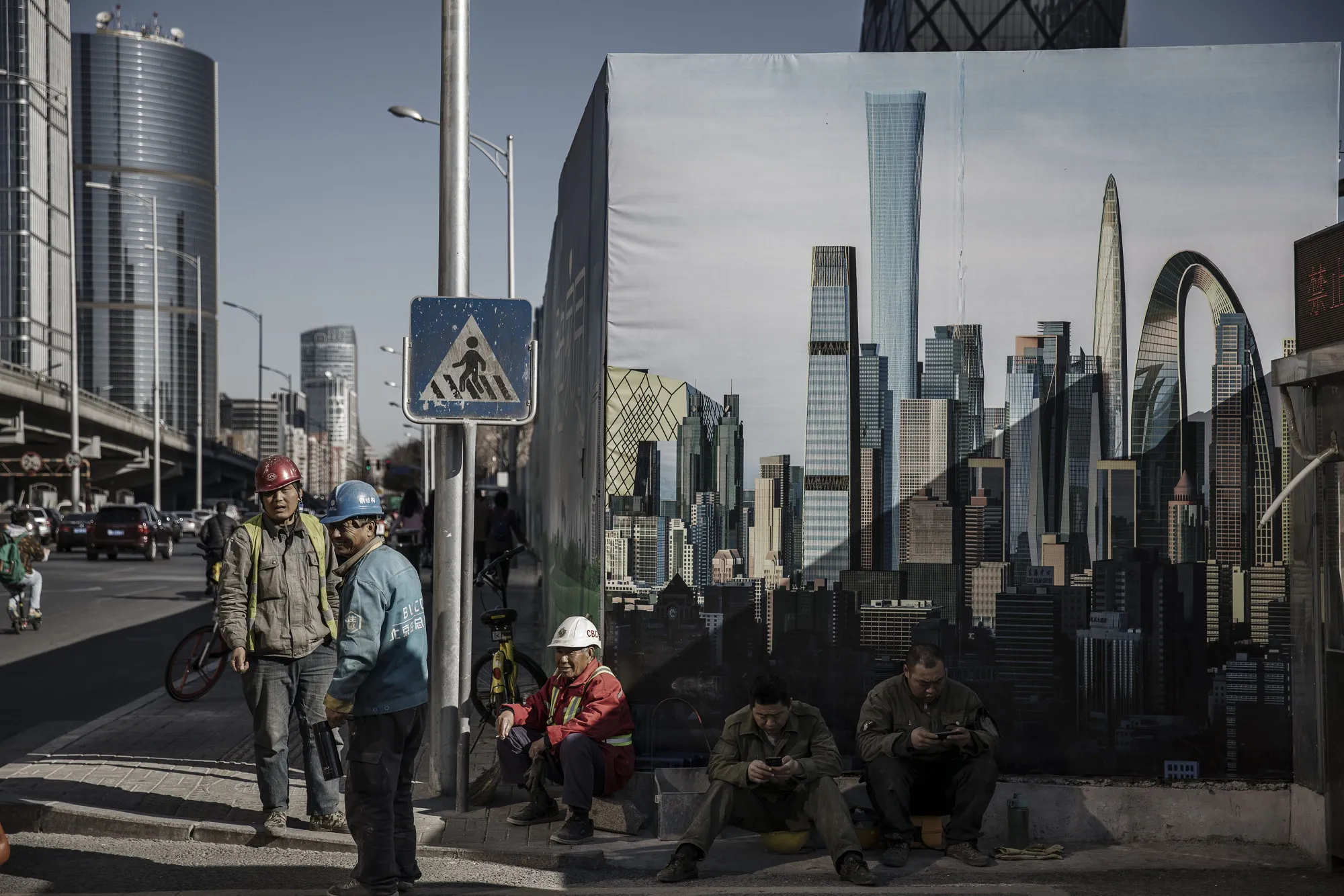 Workers stand in front of a banner featuring images of high rise towers outside a construction site in downtown Beijing.&nbsp;