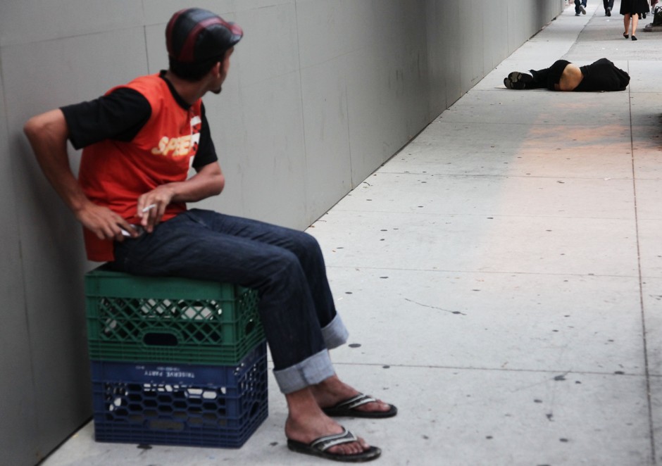 An unidentified man, left, watches Allen Duncan, who is homeless, sleep on a sidewalk in New York.