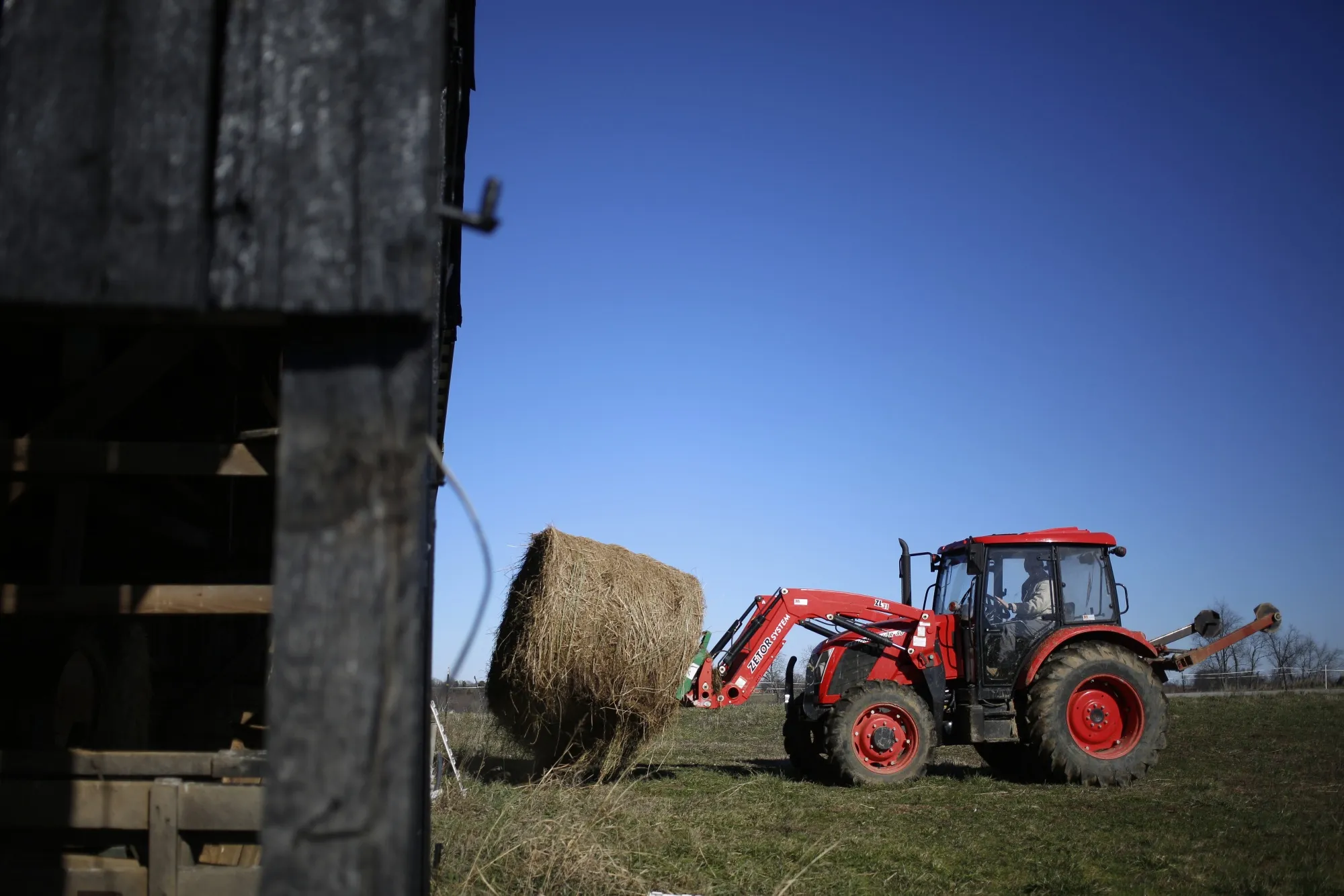 A farmer operates a tractor to transport a bale of hay at a farm in Pleasureville, Kentucky.