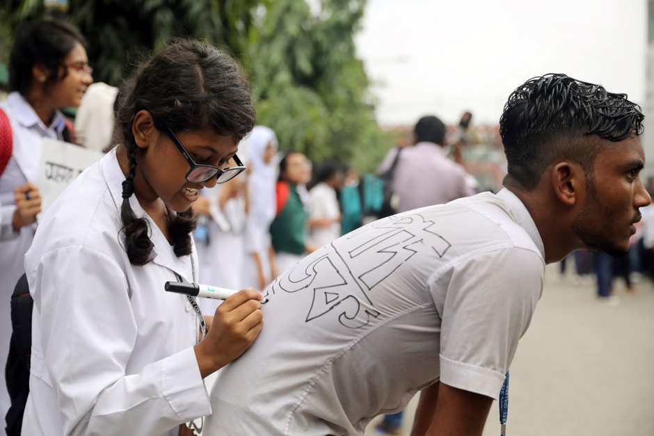 In Dhaka, a protester writes a slogan on another one's shirt during demonstrations over the death of two students in a traffic accident.