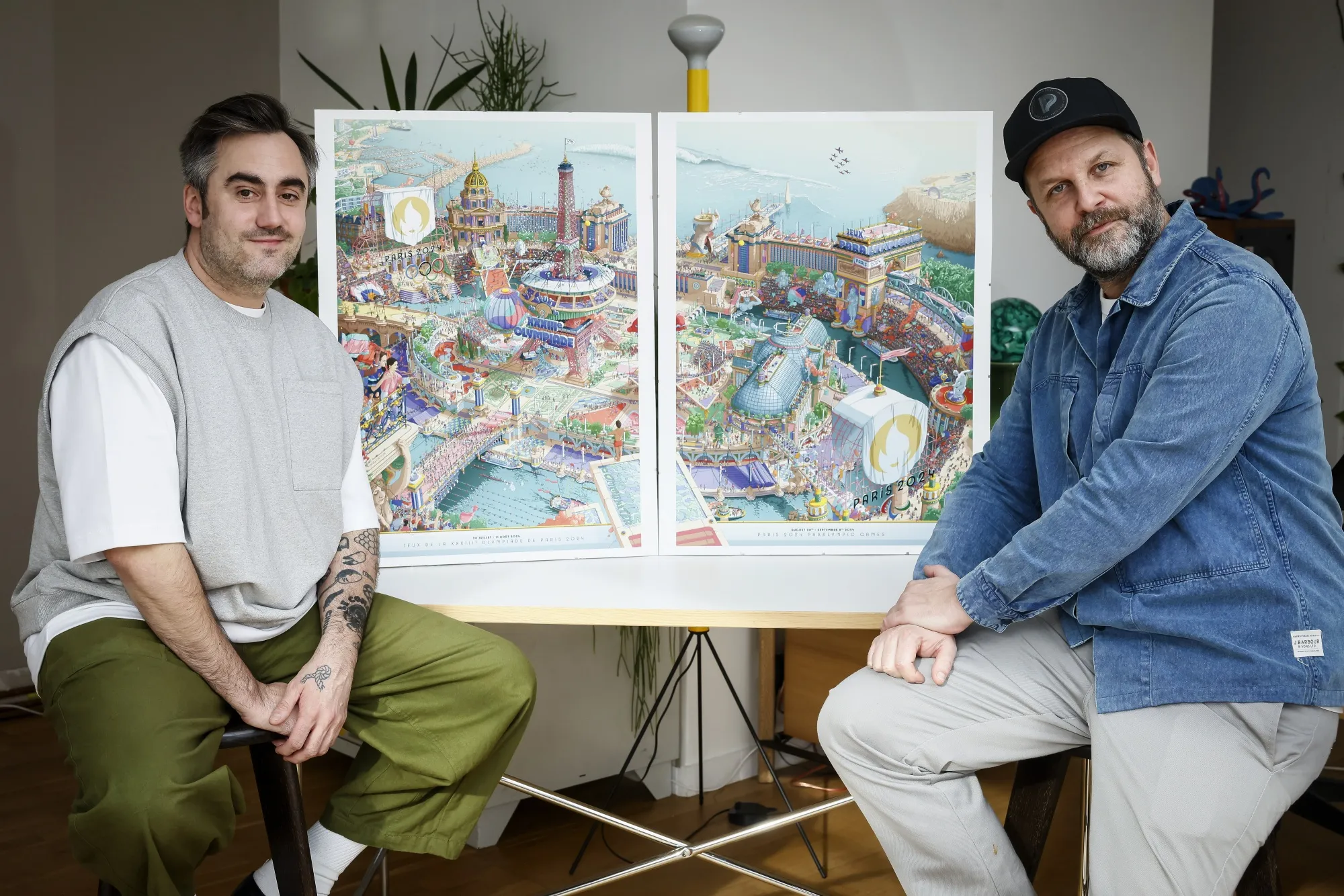 French artist Hugo Gattoni, left, and head of design for Paris 2024, Joachim Roncin pose next to the Paris 2024 Olympic and Paralympic posters in Ivry-sur-Seine outside Paris, Tuesday Feb. 20, 2024. Vibrant colors and striking landmarks illuminate posters for the Paris Olympic Games in an Art Deco style inspired by the city's flamboyant past. The posters have been unveiled at the Musée d'Orsay. (AP Photo/Thomas Padilla)