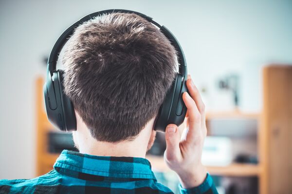RF Enjoying music at home: Young Caucasian man is listening to music with headphones, back of the head