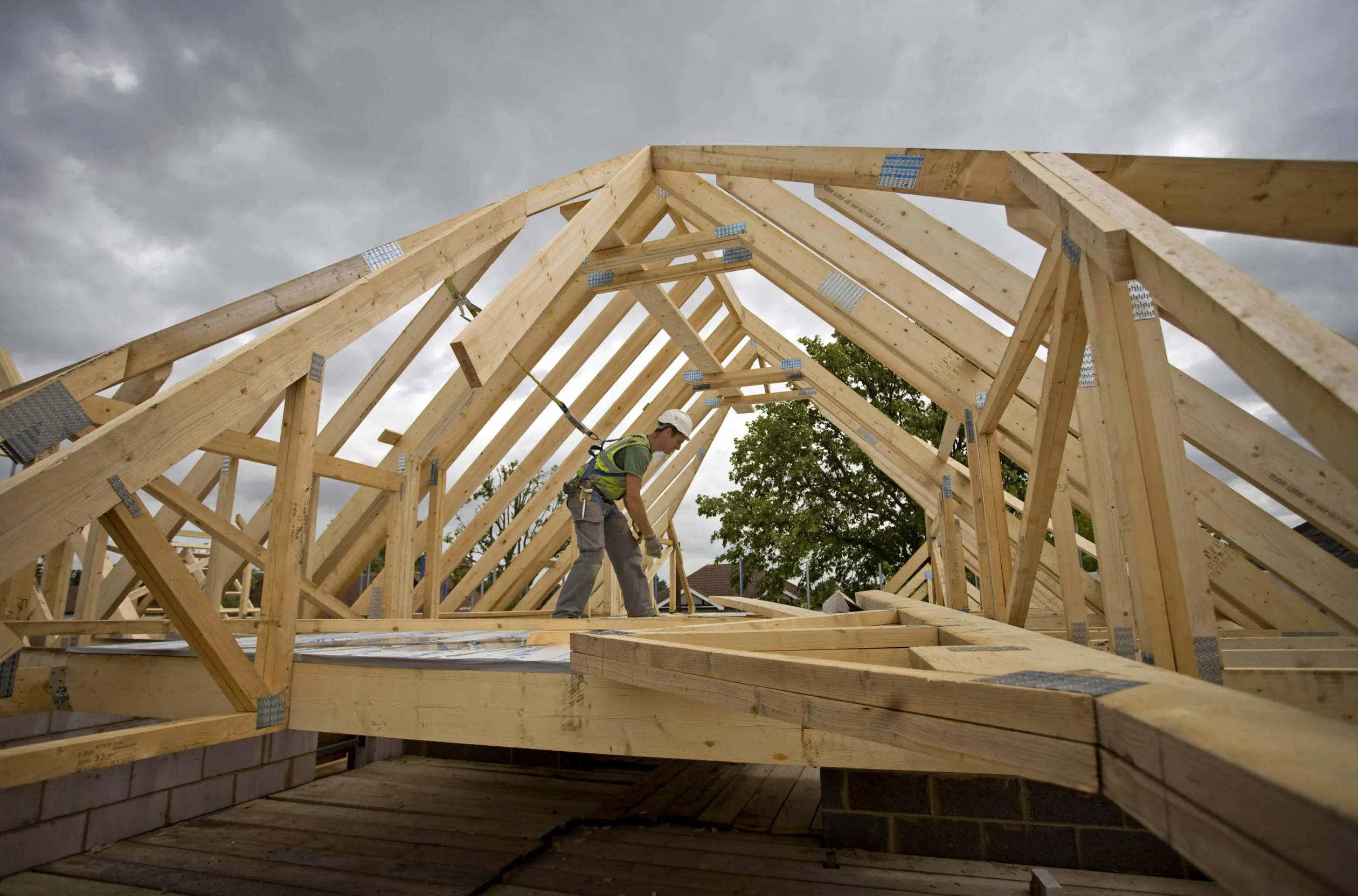 A builder lays scaffolding in a roof space on a construction site for residential housing by Kier Group Plc.