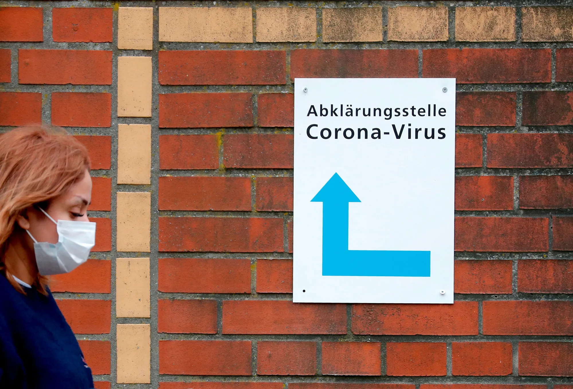 A woman walks past a sign guiding people to the entrance of a corona testing station in Berlin, on March 13.&nbsp;