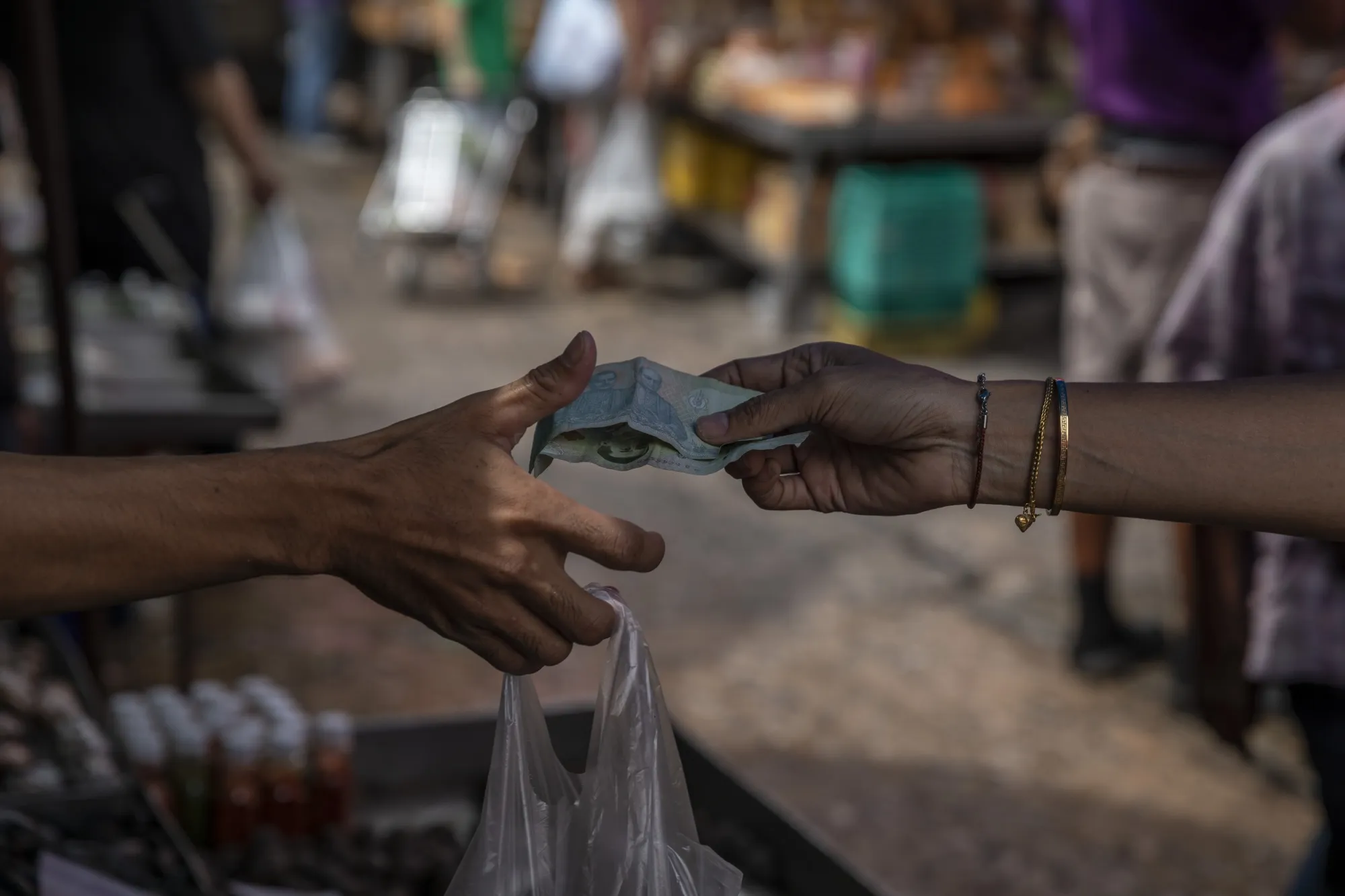 A customer hands money to a vendor at a wet market in Bangkok.