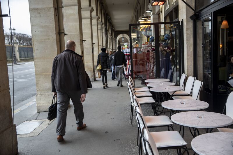 I pedoni passano tavoli vuoti in una terrazza del caffè a Parigi.