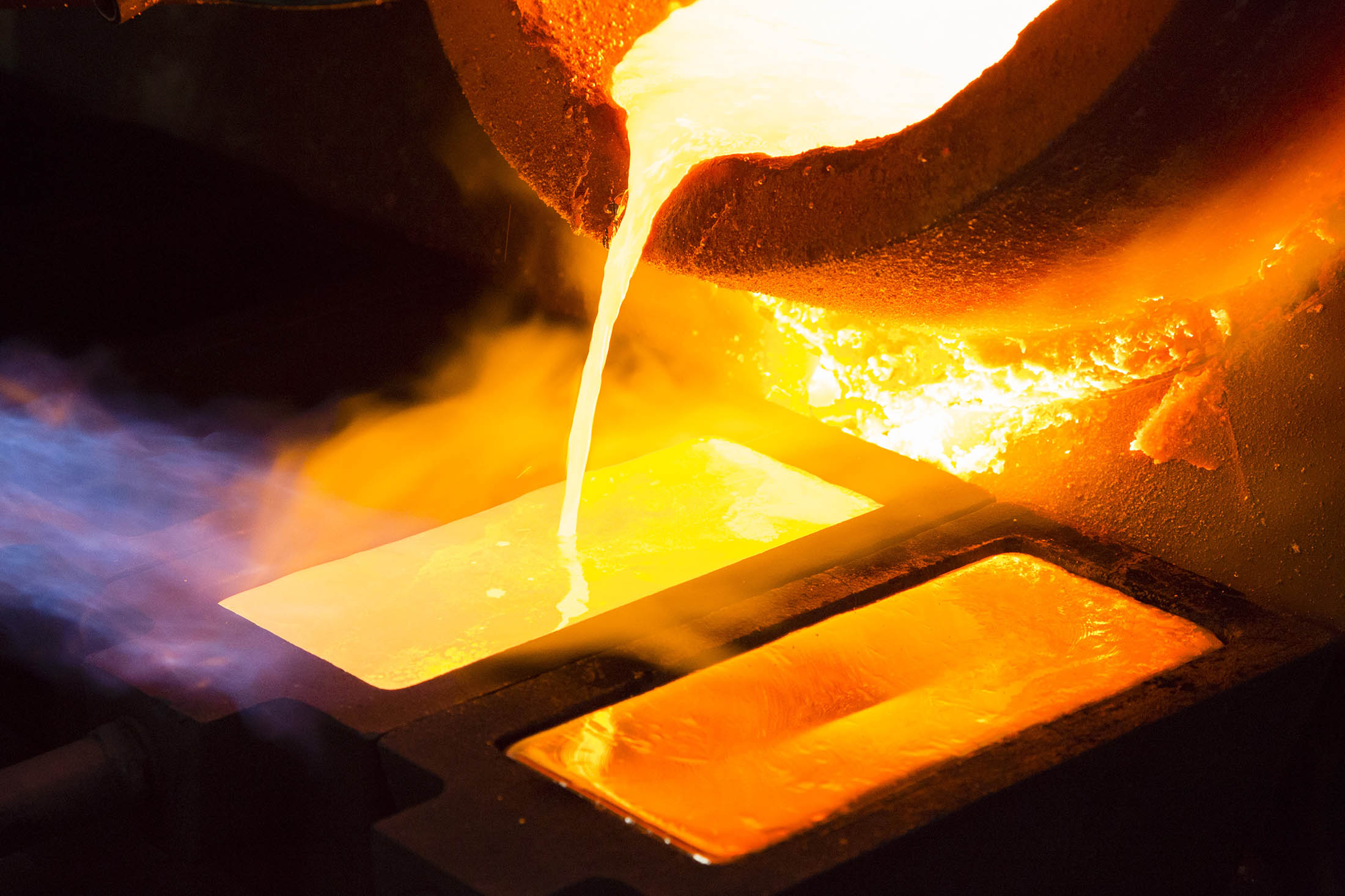 Molten gold pours from a crucible into a heated mould after refining.

