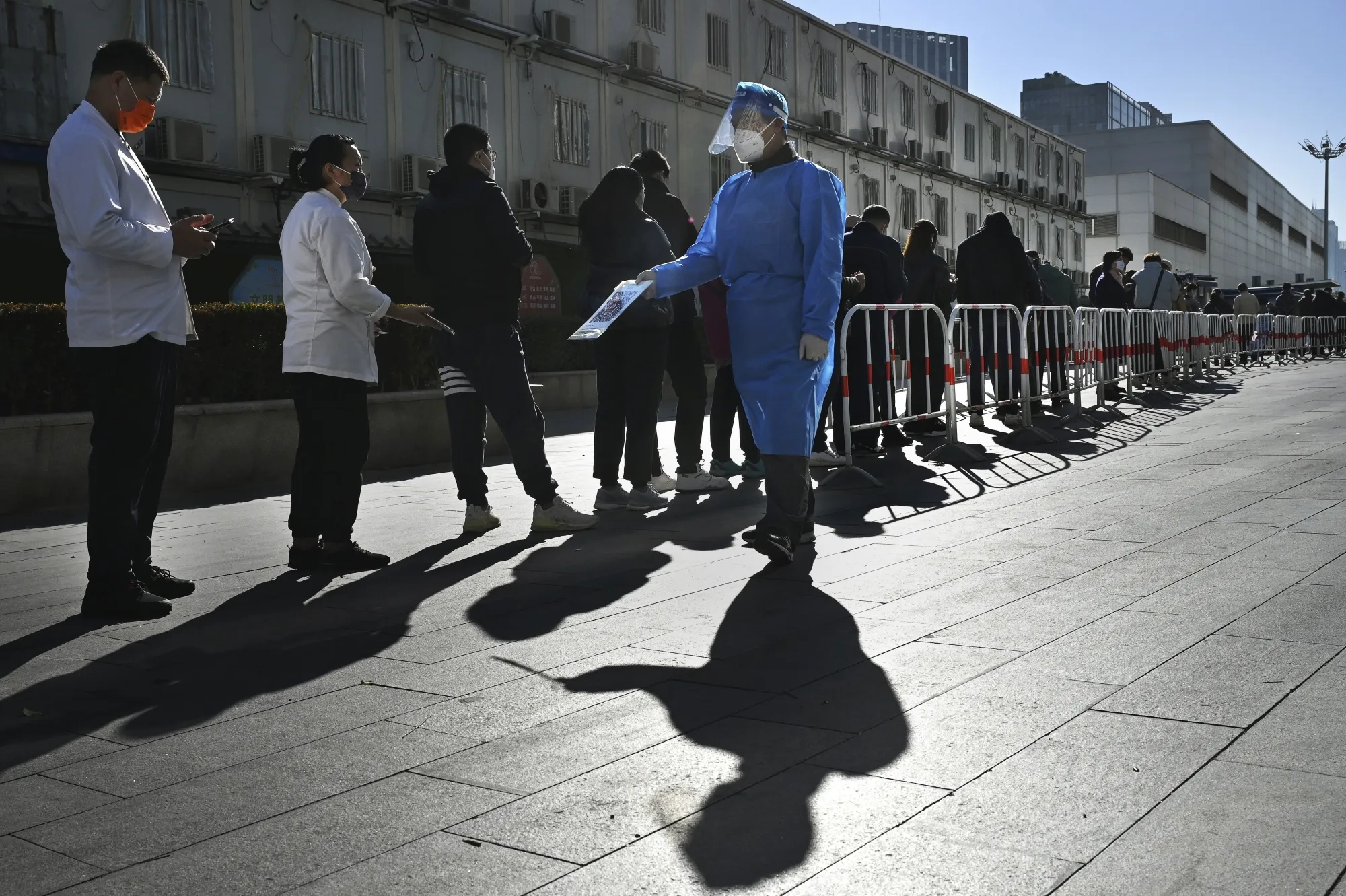 An epidemic control worker has people scan their health codes as they wait in line at a public testing site in Beijing on Nov. 15.&nbsp;