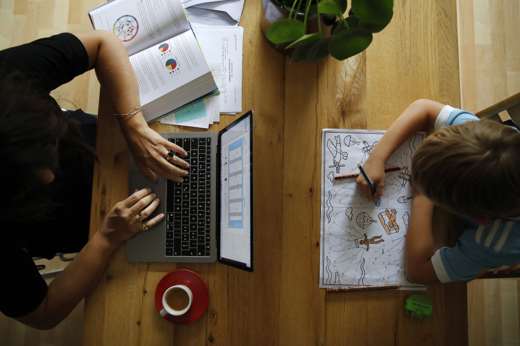 A woman works at an Apple Inc. laptop computer on a dining room table as a child sat opposite uses a coloring book in this arranged photograph taken in Bern, Switzerland, on Wednesday, Aug. 19, 2020. The biggest Wall Street firms are navigating how and when to bring employees safely back to office buildings in global financial hubs, after lockdowns to address the Covid-19 pandemic forced them to do their jobs remotely for months. Photographer: Bloomberg/Bloomberg