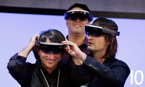 Microsoft's Joe Belfiore, left, tries on a HoloLens device with colleagues Alex Kipman, right, and Terry Myerson following an event demonstrating new features of Windows 10 at the company's headquarters on Jan. 21, 2015, in Redmond, Washington.