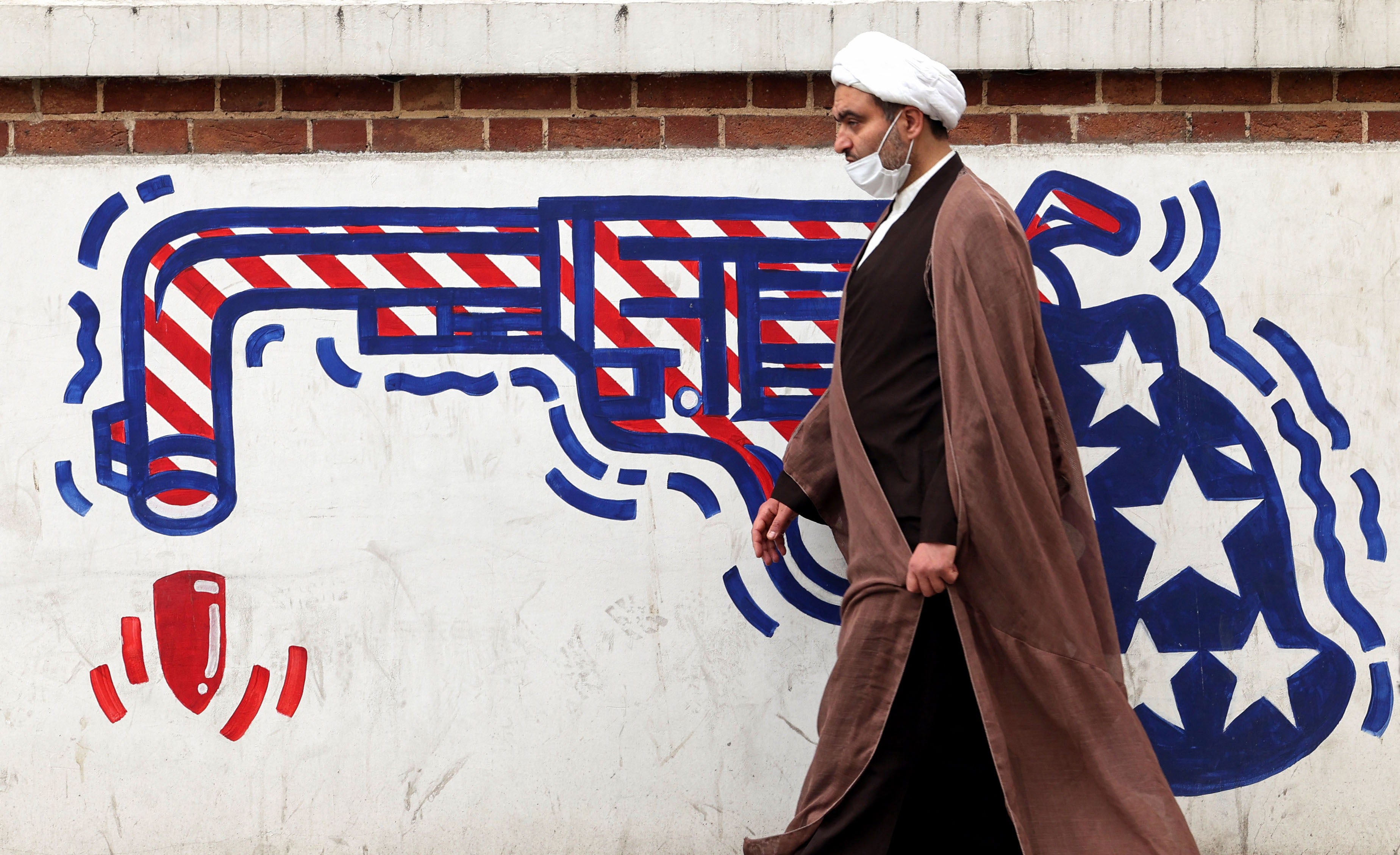 An Iranian cleric walks past an anti-US mural on a wall of the former United States embassy in the capital Tehran, on March 12, 2022. - Iran said that US attempts to seize its tankers and oil cargo had failed to stop exports that are subject to sanctions imposed by its arch foe. (Photo by ATTA KENARE / AFP) (Photo by ATTA KENARE/AFP via Getty Images)