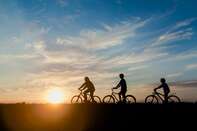 Three silhouettes on bikes riding into the sunset