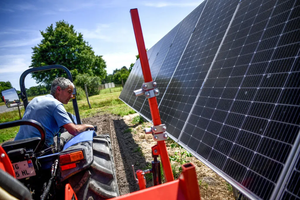 Workers use a tractor to plant seeds in a field where various crops are tested as part of a dynamic agrivoltaic project in France.