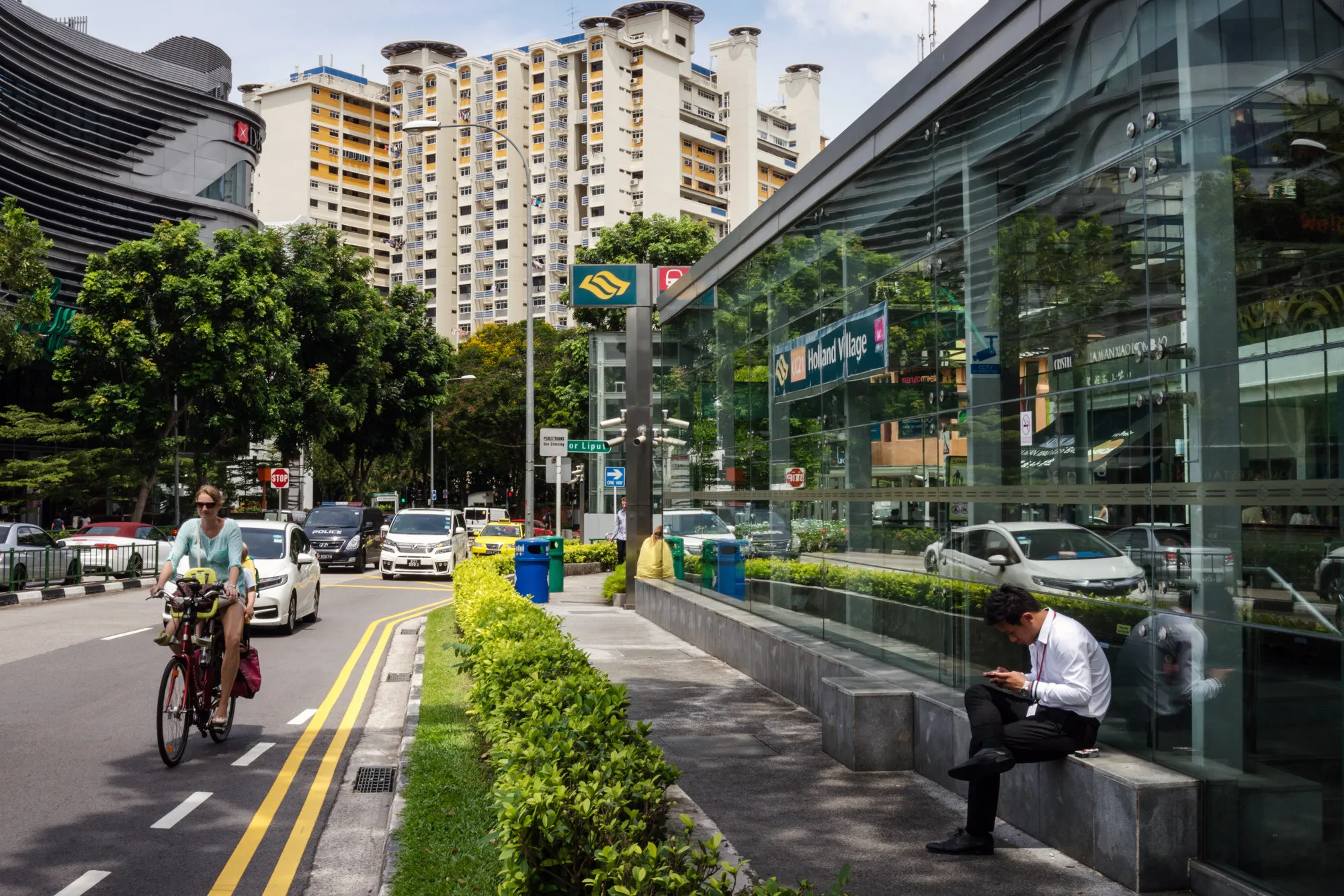 A woman rides a bicycle as a man uses a smartphone outside the SMRT Corp. Holland Village train station in the Holland Park area of Singapore, on Monday, June 5, 2017. After two years of below-par growth, economists and even Singapore's government are becoming more positive on the city-state's outlook. While it's not boom time yet, the consensus is that 2017 growth will come in higher than last year’s 2 percent.